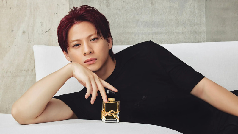 男性がYSLの香水を持ってポーズをとっている写真。彼は黒い服を着ており、髪は赤色である。