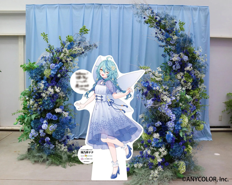 珠乃井ナナの等身大パネルが青い花で装飾されたアーチの中に立っている。