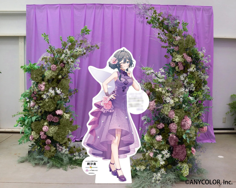 紫色のカーテンを背景に、花で飾られたアーチと、VTuberの綺沙良の等身大パネル。