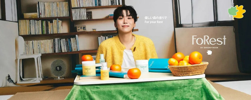 若い男性が、テーブルに置かれた様々な製品と果物、本に囲まれて座っている様子を描いた画像です。背景には本棚があり、リラックスした雰囲気を作り出しています。