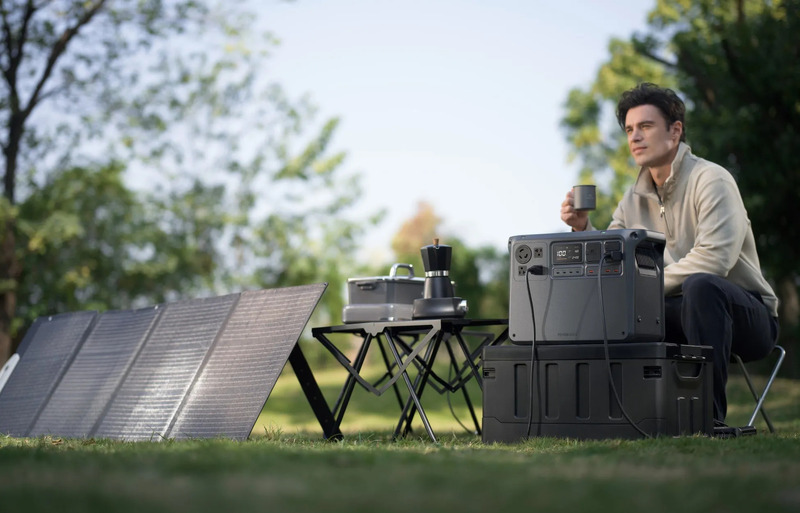 公園でコーヒーを飲みながら、ポータブル電源とソーラーパネルを使用する男性