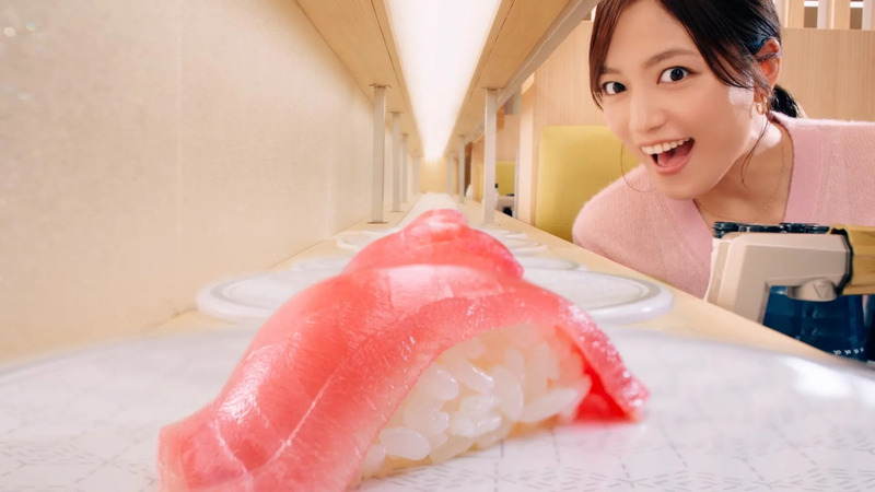 回転寿司のレーンに置かれたマグロの握り寿司を嬉しそうに見つめる女性の画像です。