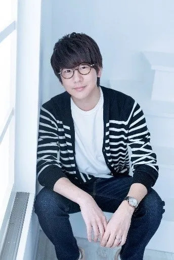 眼鏡をかけた男性が階段に座ってポーズをとっている写真です。