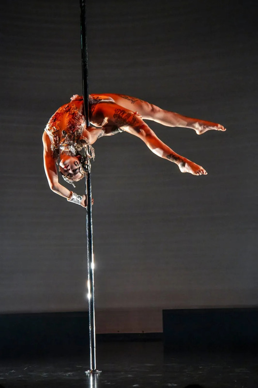 ポールダンスをしている女性。逆さまになって体を支え、アクロバティックなポーズをとっている。