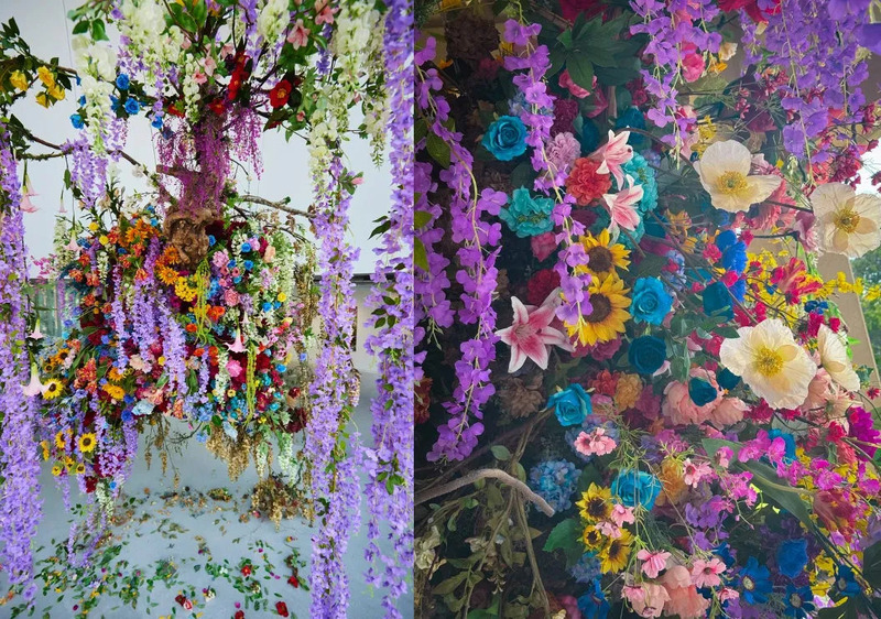 色とりどりの花々で飾られた壮大なインスタレーション。紫色の藤の花が滝のように流れ落ち、様々な色の花々が密集して芸術的な空間を作り出している。