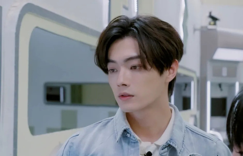 デニムジャケットを着た若いアジア人男性が真剣な表情で何かを見つめているポートレート。室内で撮影されており、背景にはモダンなデザインが見えます。