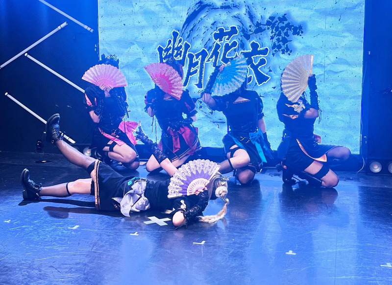 ステージでパフォーマンスをする女性グループの写真。彼女たちは扇子を持ち、伝統的な衣装を着ている。