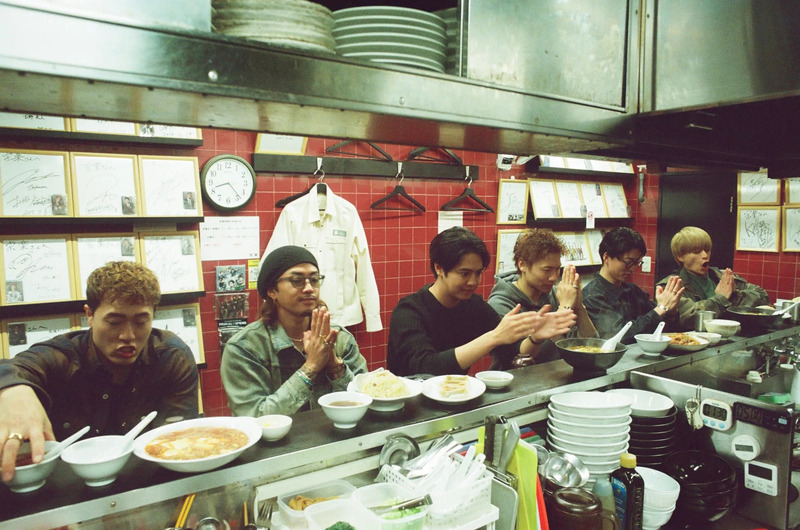 ラーメン屋で食事をする男性グループの写真。彼らは手を合わせて食事に感謝している様子。