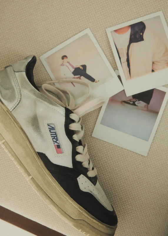 白いスニーカーとポラロイド写真の静物写真。スニーカーは、黒、白、銀色のデザインで、AUTRYのロゴとアメリカ国旗が付いています。ポラロイド写真は、人が写っているものと、スニーカーを履いている人の足元を写したものの2種類です。