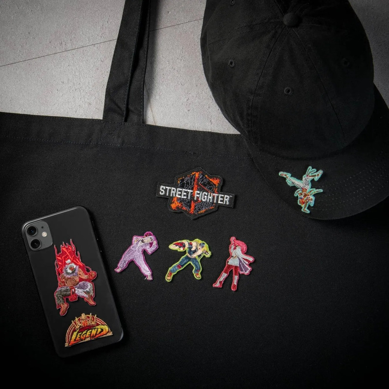黒いトートバッグ、帽子、スマートフォン、ワッペンが写っている画像。バッグには「STREET FIGHTER」のワッペンと、キャラクターのワッペン、スマートフォンにはキャラクターのワッペンと「LEGEND」の文字が見える。