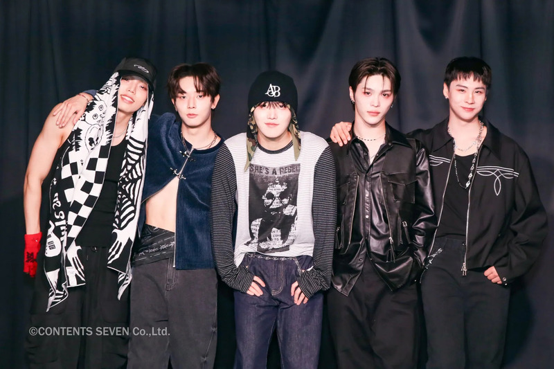 5人の男性グループのポートレート。彼らは様々なファッションスタイルを身につけており、背景は黒。