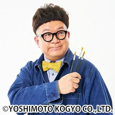 眼鏡をかけた男性が、蝶ネクタイとブラシを持ってカメラ目線で微笑んでいる写真です。