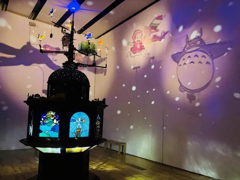 スタジオジブリのキャラクターの影絵が壁に映し出された展示。中央にはステンドグラスのあるオブジェが置かれ、幻想的な空間を演出している。