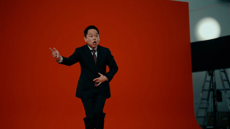 赤い背景の前で、スーツを着た男性が驚いた表情でポーズをとっている様子を捉えた写真です。