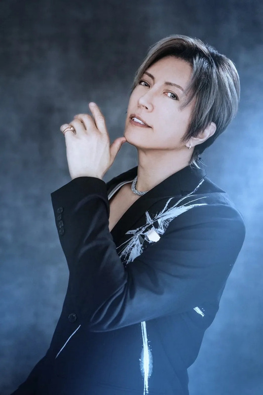 黒いジャケットを着た男性のポートレート。彼は指で顎に触れ、カメラを見ている。