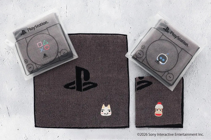 PlayStationのロゴやキャラクターがデザインされたタオルセットの写真です。タオルはグレーで、PlayStationのコントローラーやロゴが刺繍されています。また、猫や靴下のキャラクターの刺繍も施されています。