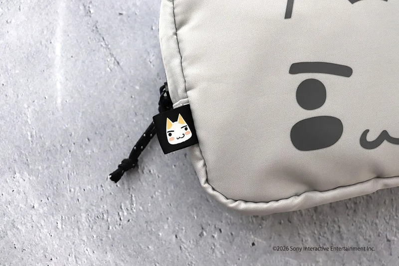 猫の顔が描かれたタグが付いたグレーのポーチのクローズアップ。ポーチには顔の模様が描かれており、背景はグレーの表面。