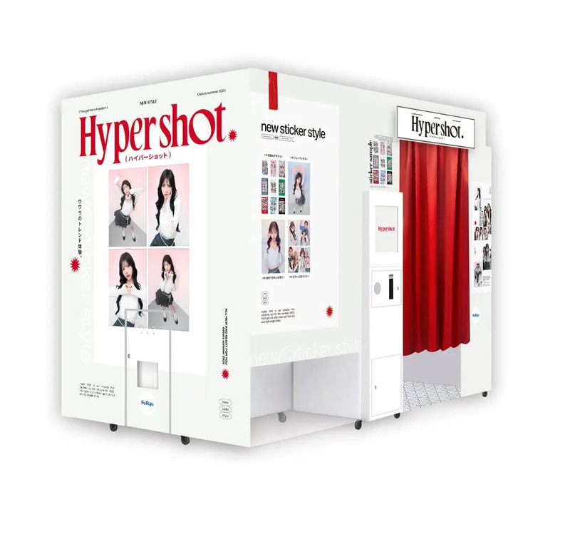 白い筐体に「Hypershot」のロゴが入った、写真撮影機。赤いカーテンが特徴的で、若い女性の写真やサンプルのステッカーが展示されている。