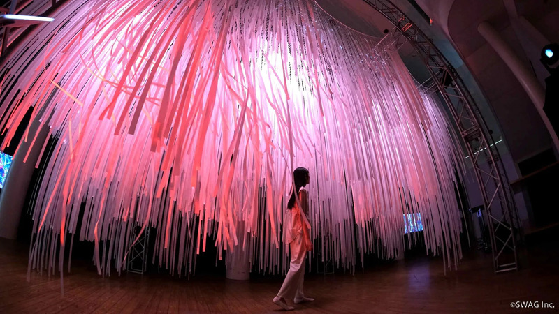 ピンク色の光に照らされた空間に、女性が歩いている様子。