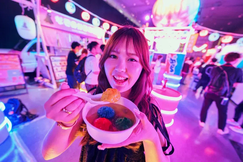 女性がカラフルなデザートを手に持ち、笑顔でカメラを見ている