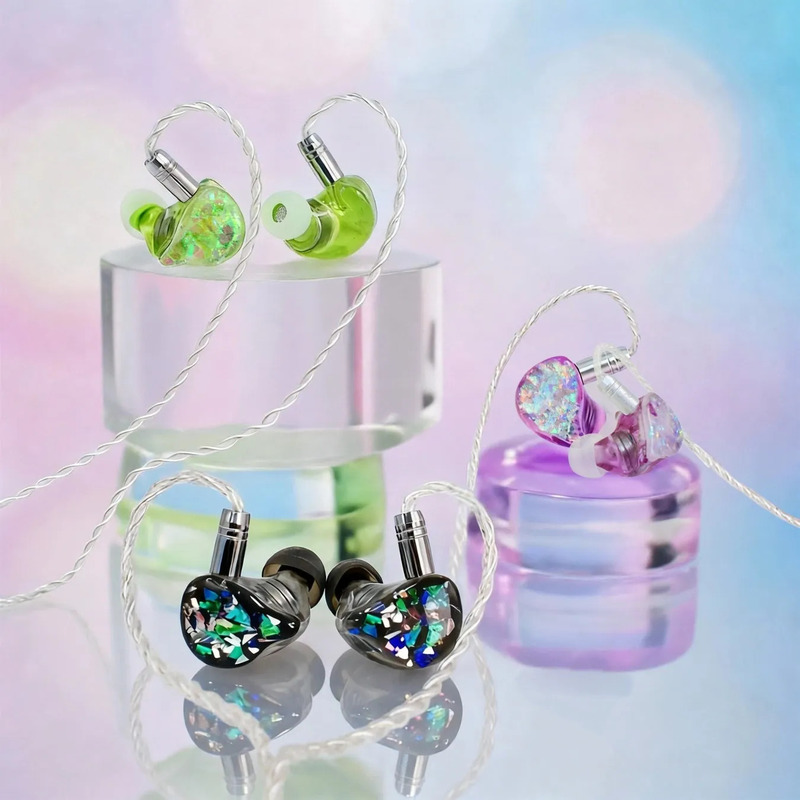 透明な台座に置かれた、さまざまな色のインイヤーイヤホンのクローズアップ写真。イヤホンは、緑、紫、黒のさまざまな色合いで表示されます。