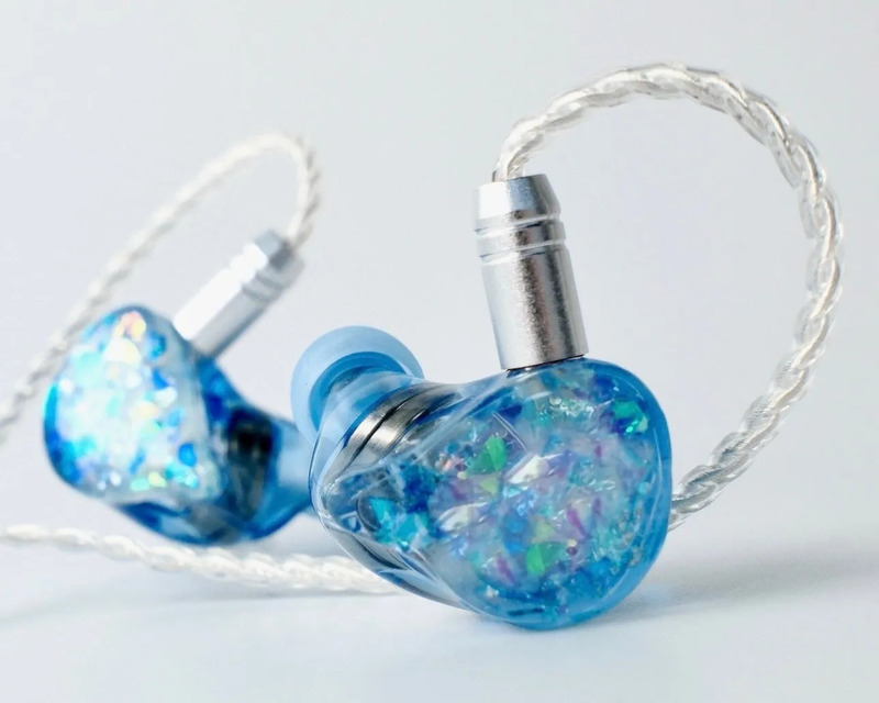 青色のイヤホンが2つ並んだ写真。イヤホンはキラキラしたデザインで、ケーブルは白っぽい色をしている。