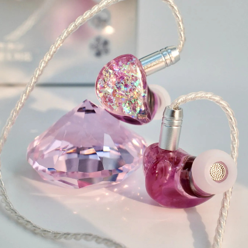 ピンク色のイヤホンとピンク色のダイヤモンド型のオブジェが置かれた写真です。イヤホンはキラキラした装飾が施されており、高級感があります。
