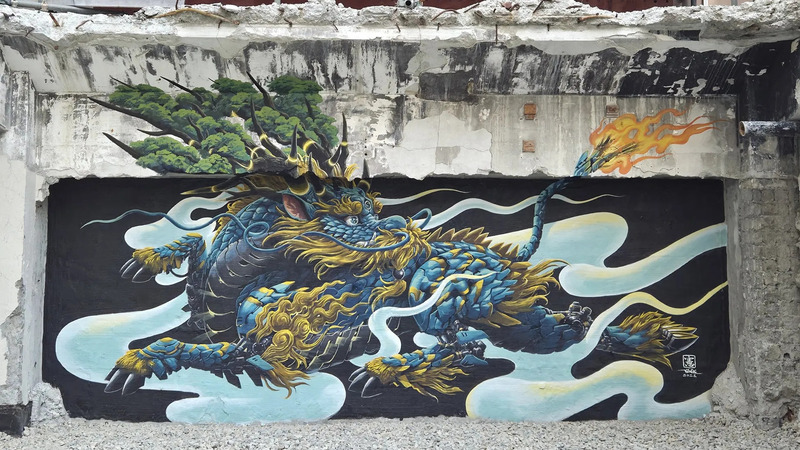壁に描かれた青と金の龍の壁画。龍は大きく、今にも動き出しそうな姿で描かれている。背景は黒で、白い雲のような模様が描かれている。龍の周りには炎のようなものが描かれ、迫力ある印象を与えている。
