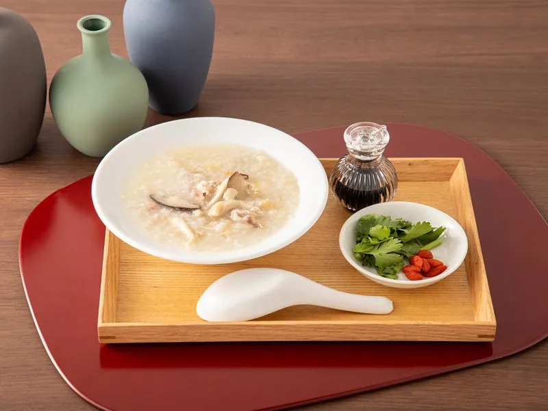 白い器に入ったお粥が写っている。薬味と醤油も添えられており、食卓を彩る様子が写っている。