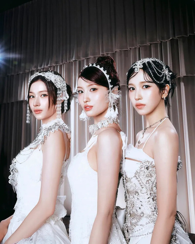 3人の女性が白いドレスを着てポーズをとっている写真。女性たちはそれぞれ異なるヘアスタイルをしており、華やかなアクセサリーを身につけている。背景はカーテンで、照明が当たっている。