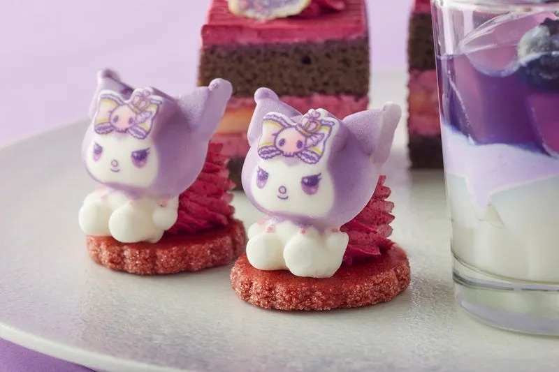 紫色のキャラクターの形をしたデザートが2つ、赤いクリームとクッキーの上に置かれています。ケーキとデザートが入ったグラスも写っています。